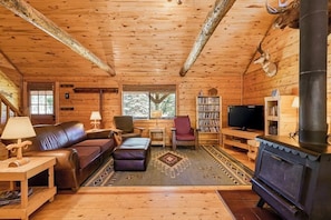 A log cabin interior with a fireplace, leather sofa, armchairs, a TV, and a bookshelf. - Dog-Friendly Cabin w/ Washer/Dryer, WiFi, & Firepit - Steps From the Rio Grande (South Fork)