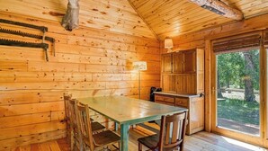 A wooden cabin interior with a dining table, chairs, a kitchen area, and a large window. - Dog-Friendly Cabin w/ Washer/Dryer, WiFi, & Firepit - Steps From the Rio Grande (South Fork)