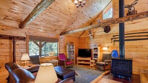 A log cabin interior with a fireplace, leather sofa, television, bookshelves, and a deer head mounted on the wall. - Dog-Friendly Cabin w/ Washer/Dryer, WiFi, & Firepit - Steps From the Rio Grande (South Fork)