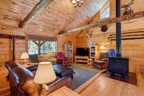 A log cabin interior with a fireplace, leather sofa, television, bookshelves, and a deer head mounted on the wall. - Dog-Friendly Cabin w/ Washer/Dryer, WiFi, & Firepit - Steps From the Rio Grande (South Fork)