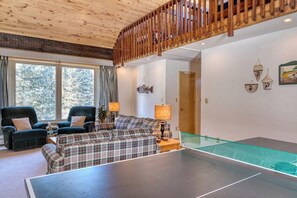 Ein Wohnzimmer mit Tischtennisplatte, zwei Sesseln, einer Couch und einer Holzbalkendecke.