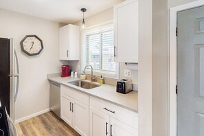 Eine Küche mit weißen Schränken, einer Spüle, einem Toaster und einer Uhr an der Wand.