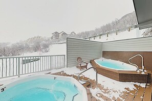 Ein Whirlpool und ein Schwimmbad auf einer verschneiten Terrasse mit Blick auf Häuser im Hintergrund.