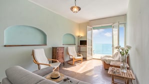 A room with a sofa, two rocking chairs, a small table with a vase and flowers, and a view of the sea through an open door. - Attico Giancardi - Beachfront Sea-View Terrace, Alassio, Italy (Alassio)