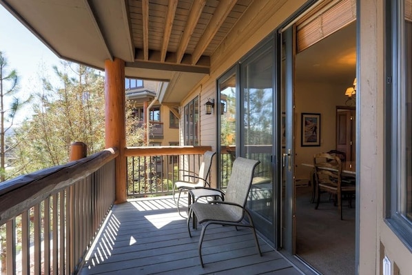A wooden deck with chairs, a glass door leading to an interior dining area, and a view of trees. - Ski-in/out mountain condo with W/D, free WiFi, pool, & hot tub (Steamboat Springs)