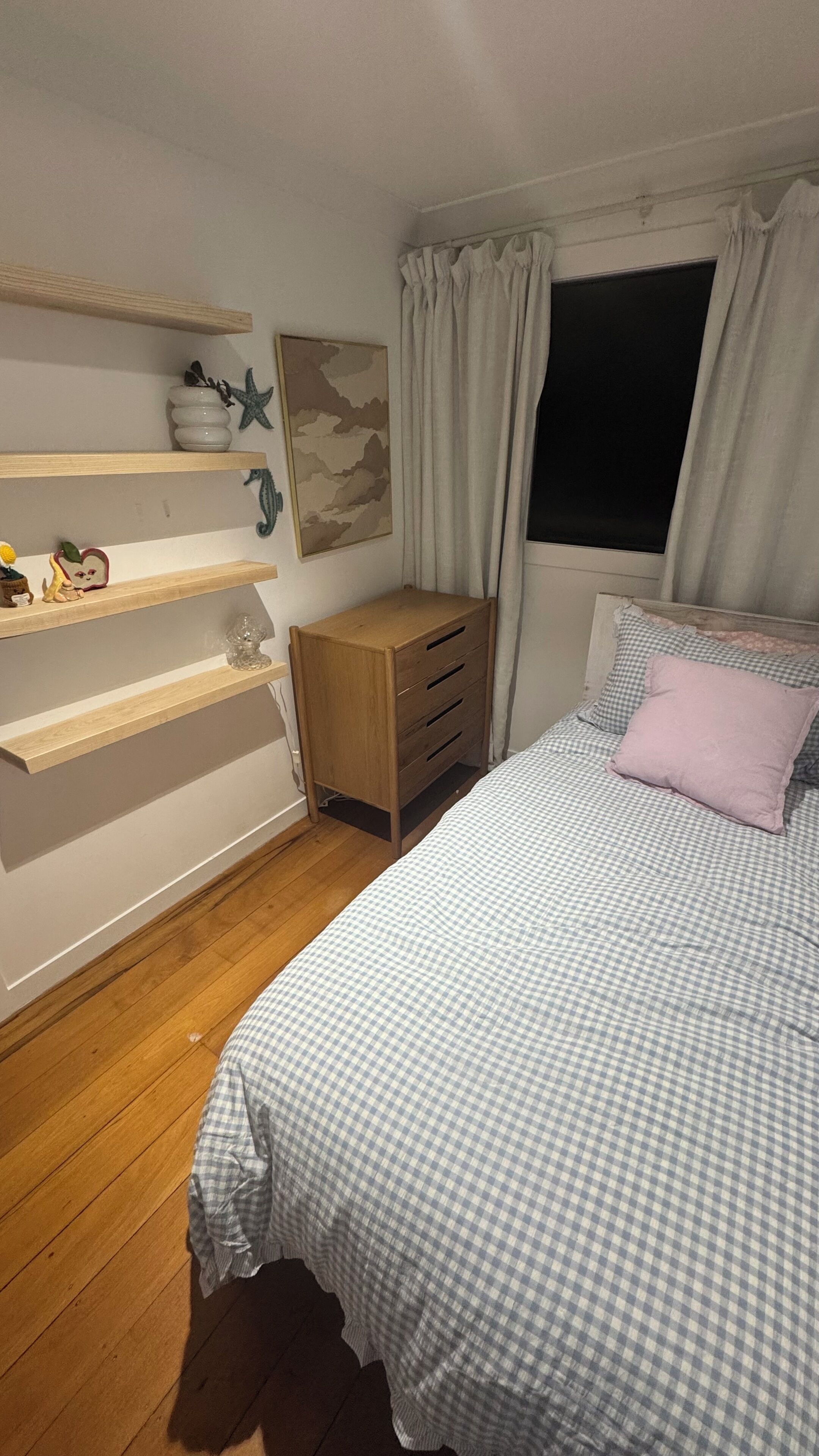 A bedroom with a bed, wooden dresser, shelves, and a window with curtains.. Bach over the bay