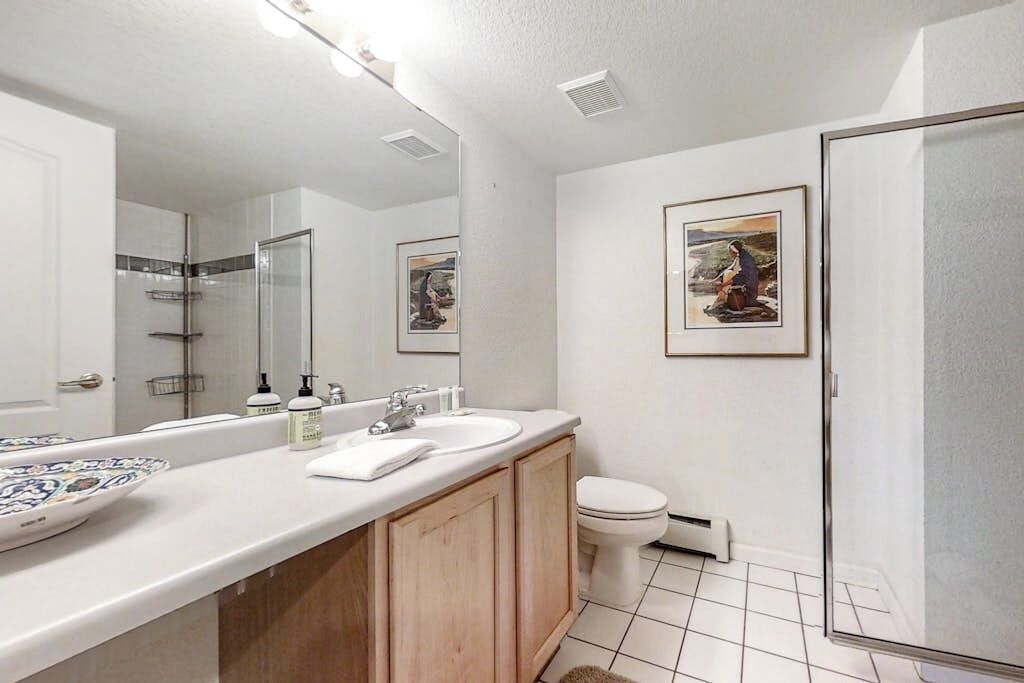 A bathroom with a white sink, mirror, and toilet, with two framed pictures on the wall.