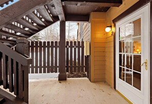 Eine überdachte Veranda mit Holzzaun, einer Tür mit Glasfeldern und einer Leuchte.