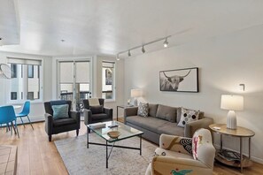 Ein modernes Wohnzimmer mit einem Glastisch, zwei Sofas, einem Essbereich mit Stühlen und einem großen Fenster.