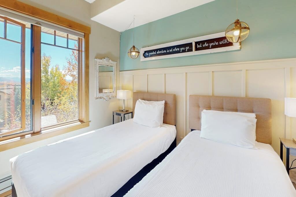 Een hotelkamer met twee bedden, een groot raam met uitzicht, een spiegel aan de muur en een decoratief bord.