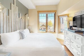 Ein Schlafzimmer mit einem großen Bett, einem Schminktisch, einem Fernseher und einem Fenster mit Blick auf Gebäude.