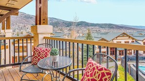 En balkon med bord og stole, der udover et smukt udsigtspunkt over et dalområde og et vandareal.