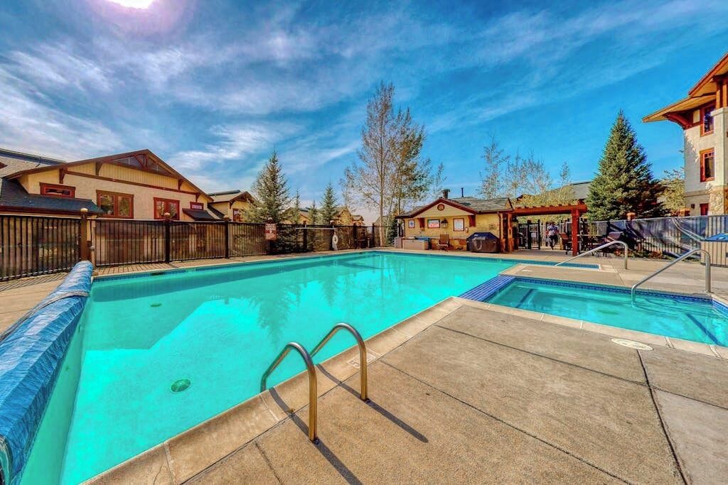A swimming pool with a clear blue water, surrounded by a fence, and adjacent to buildings with a wooden facade.