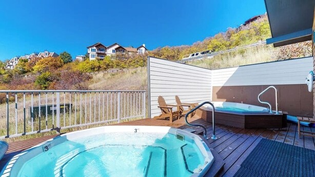 Ein Whirlpool auf einer Holzdielen-Terrasse mit Blick auf Häuser und Bäume.