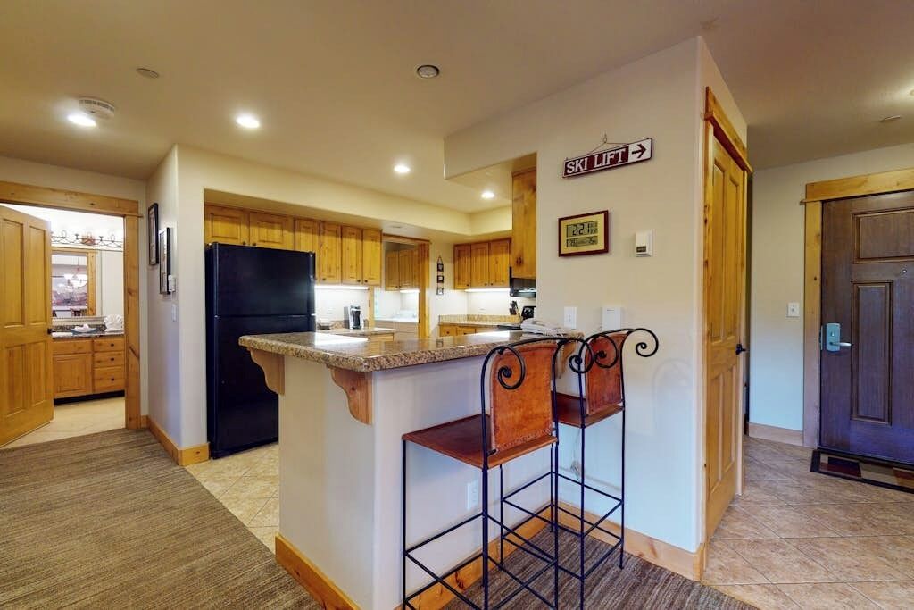 A kitchen with wooden cabinets, a black refrigerator, a granite countertop, and two bar stools.