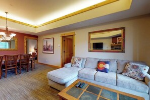 Ein Wohnzimmer mit einer Couch, einem Couchtisch, einem Esstisch mit Stühlen, einer Kristallleuchtre und einem großen Spiegel.