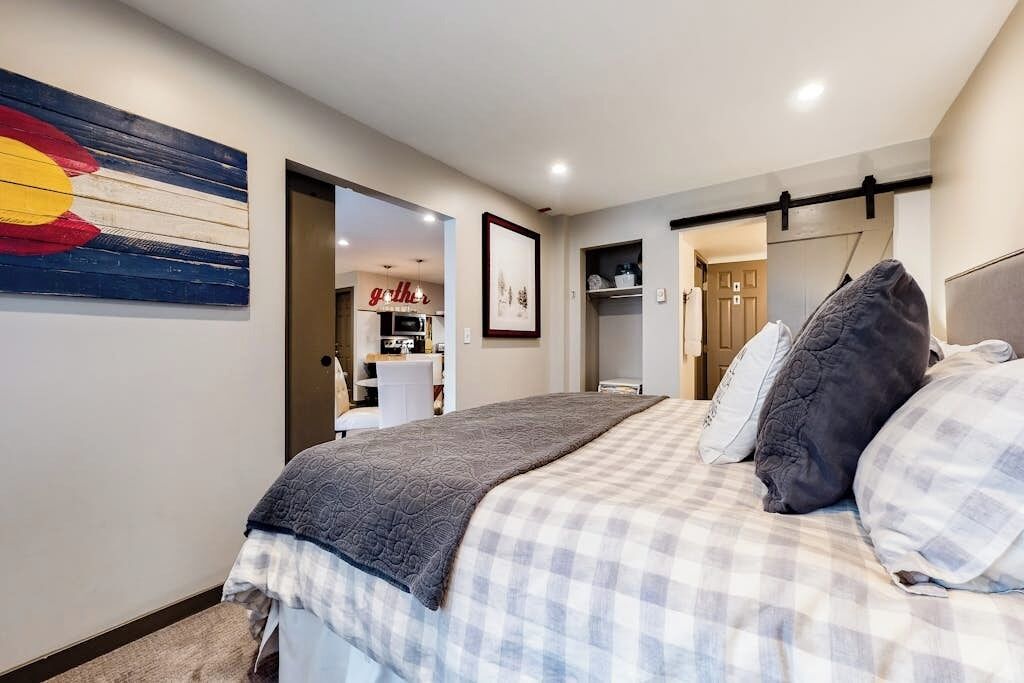 A bedroom with a bed, a wall-mounted artwork, a door leading to a bathroom, and a hallway.
