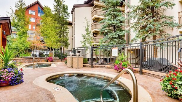 Un espace avec un jacuzzi et une piscine, entouré d’une clôture, et un immeuble à plusieurs étages en arrière-plan.