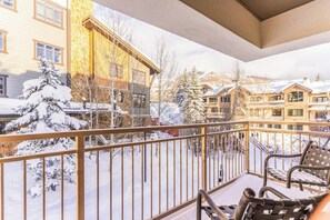 A balcony with a view of snow-covered buildings and trees. - Mountain view condo w/ fireplace, W/D, shared hot tubs/firepit, steps to gondola (Steamboat Springs)
