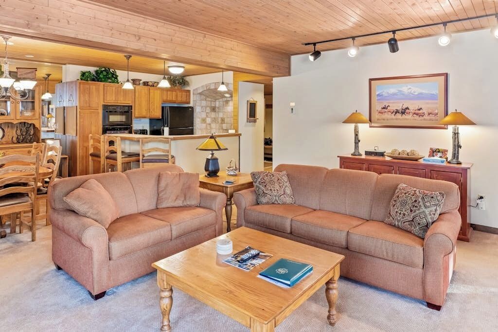 A living room with a sofa set, a coffee table, and a kitchen area in the background.