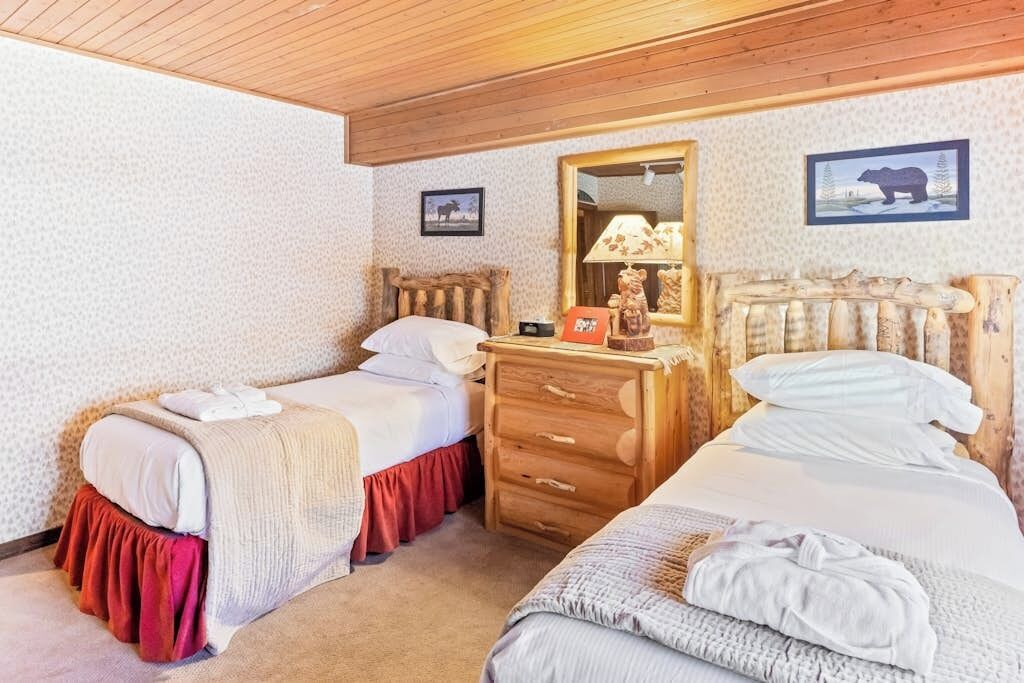 Une chambre avec deux lits, une commode en bois, un miroir et une lampe.