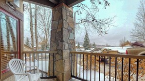 A balcony with a stone pillar, a white plastic chair, and a view of a snowy landscape with trees and a parked car. - Walk-to-gondola condo w/ fireplace, W/D & resort pool/hot tubs/shuttle/gym (Steamboat Springs)