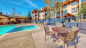 A pool area with a table and chairs, a covered seating area, and a building with multiple balconies. - Walk-to-gondola condo w/ fireplace, W/D & resort pool/hot tubs/shuttle/gym (Steamboat Springs)