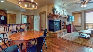 A spacious living area with a wooden dining table, black chairs, a fireplace, and a ceiling fan. - Walk-to-gondola condo w/ fireplace, W/D & resort pool/hot tubs/shuttle/gym (Steamboat Springs)