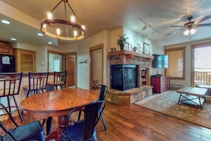 A spacious living area with a wooden dining table, black chairs, a fireplace, and a ceiling fan. - Walk-to-gondola condo w/ fireplace, W/D & resort pool/hot tubs/shuttle/gym (Steamboat Springs)