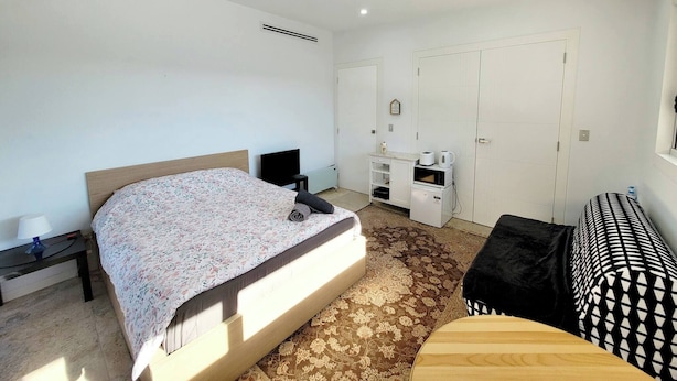 Ein Schlafzimmer mit Bett, Nachttisch, Lampe, Kleiderschrank und einer kleinen Sitzecke.