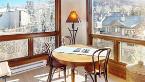 Un'area pranzo con tavolo e sedie, una lampada e ampie finestre che offrono vista su edifici e alberi.