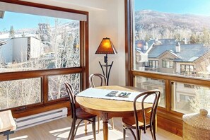 Ein Essbereich mit Tisch und Stühlen, einer Lampe und großen Fenstern mit Blick auf Gebäude und Bäume.