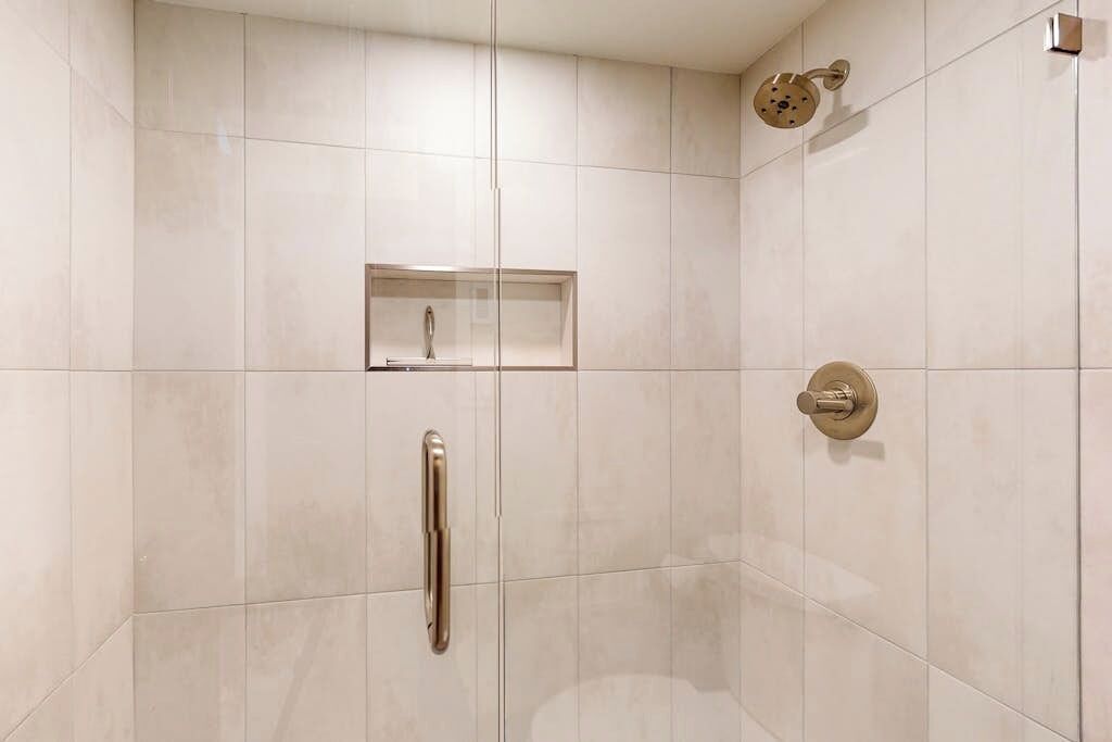 Un baño moderno con ducha, lavamanos con mampara de vidrio y un inodoro.