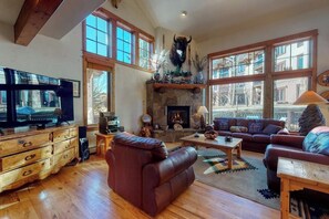 A spacious living room with a fireplace, leather sofa, wooden coffee table, and large windows. - Large townhouse with heated pool, shared hot tub, & balcony - walk to gondola (Steamboat Springs)