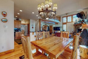 A spacious dining area with a large wooden table and chairs, a chandelier, and a fireplace. - Large townhouse with heated pool, shared hot tub, & balcony - walk to gondola (Steamboat Springs)