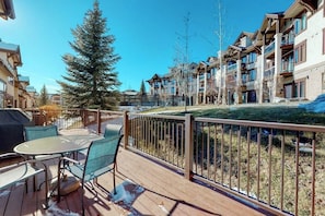 A wooden deck with outdoor furniture, a metal railing, and a view of multi-story buildings with balconies. - Large townhouse with heated pool, shared hot tub, & balcony - walk to gondola (Steamboat Springs)