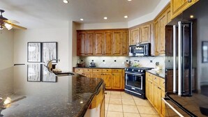 A kitchen with wooden cabinets, a black countertop, a stove, a microwave, and a refrigerator. - Walk-to-lift townhome w/ fireplace, laundry & resort pool/hot tubs/gym/firepit (Steamboat Springs)