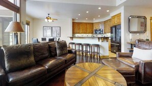 A spacious living area with a leather sofa, round coffee table, and a kitchen with wooden cabinets and a refrigerator. - Walk-to-lift townhome w/ fireplace, laundry & resort pool/hot tubs/gym/firepit (Steamboat Springs)