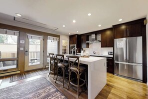 A modern kitchen with dark wood cabinets, stainless steel appliances, and a central island with bar stools. - Upscale chic condo close to slopes with hot tubs & winter shuttle (Steamboat Springs)