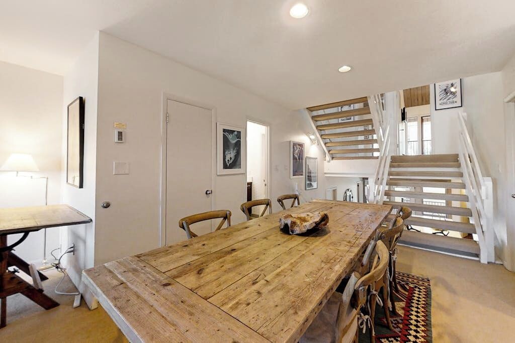 A dining area with a wooden table and chairs, a staircase, and framed artwork on the walls.