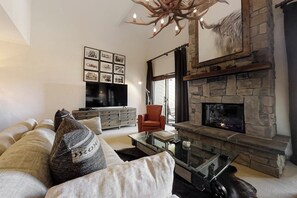 A living room with a stone fireplace, a sofa, a red chair, and a flat-screen TV mounted on the wall. - Upscale chic condo close to slopes with hot tubs & winter shuttle (Steamboat Springs)