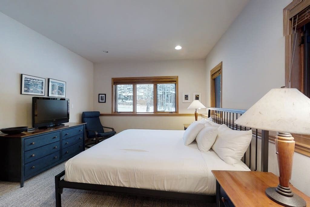 A bedroom with a bed, a TV, a desk, and a window.