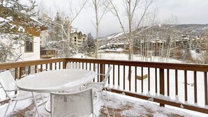 A snow-covered deck with a table and chairs, overlooking a residential area with houses and trees. - Evergreen 03 Luxurious Townhome Featuring a Shared Pool and Shuttle (Steamboat Springs)