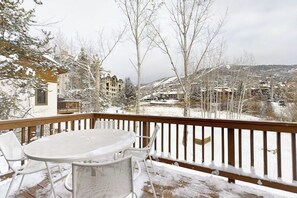 A snow-covered deck with a table and chairs, overlooking a residential area with houses and trees. - Luxurious Townhome Featuring a Shared Pool and Shuttle (Steamboat Springs)