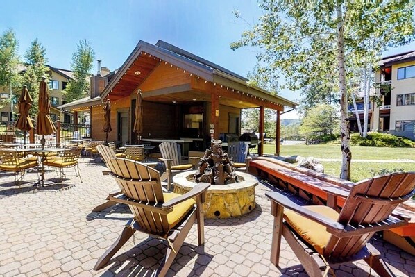 Eine Terrasse im Freien mit Holzmöbeln, einem Feuerkorb und einer überdachten Sitzgruppe.