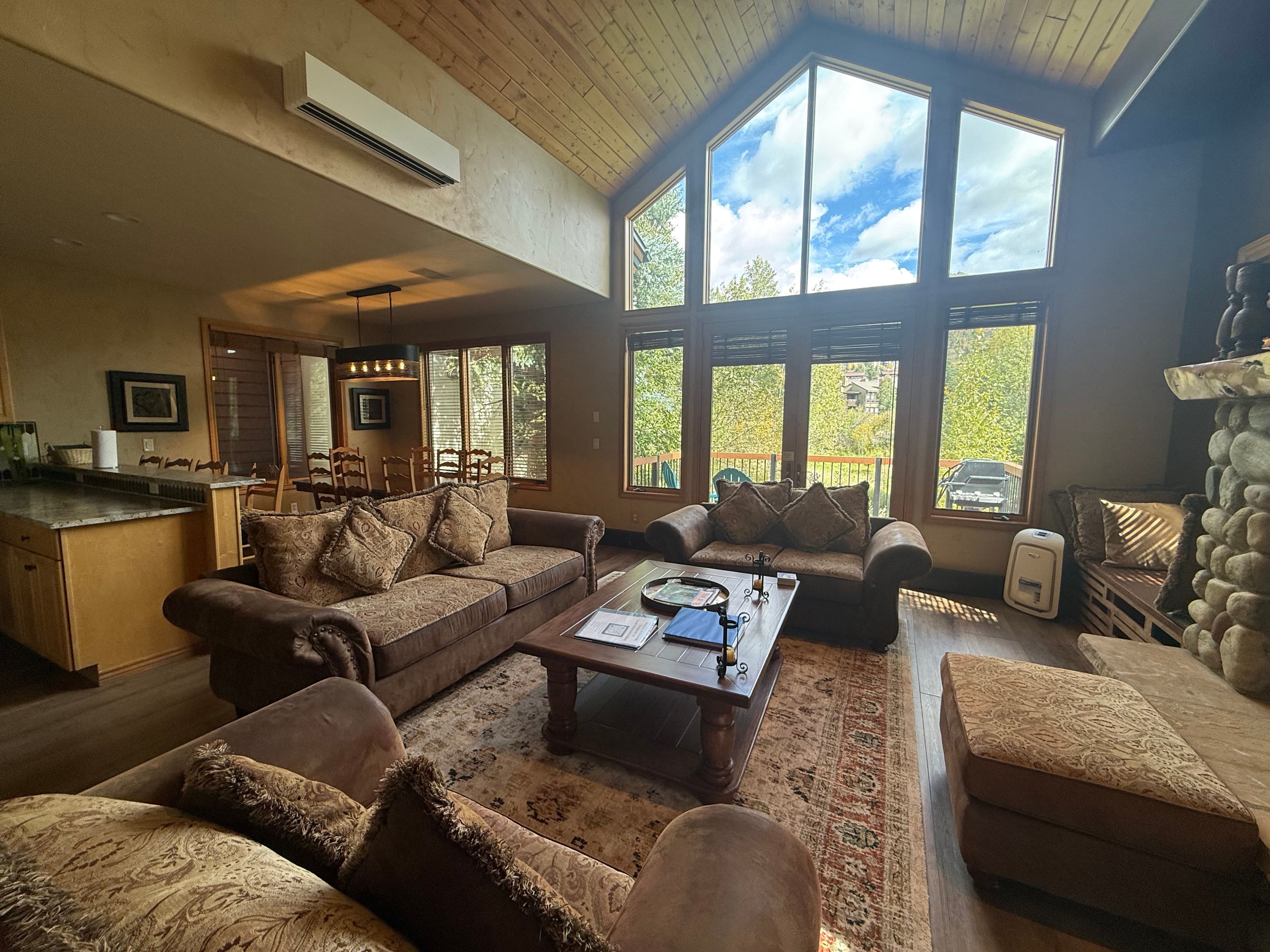 A spacious living area with a large window, a fireplace, and a kitchen in the background.