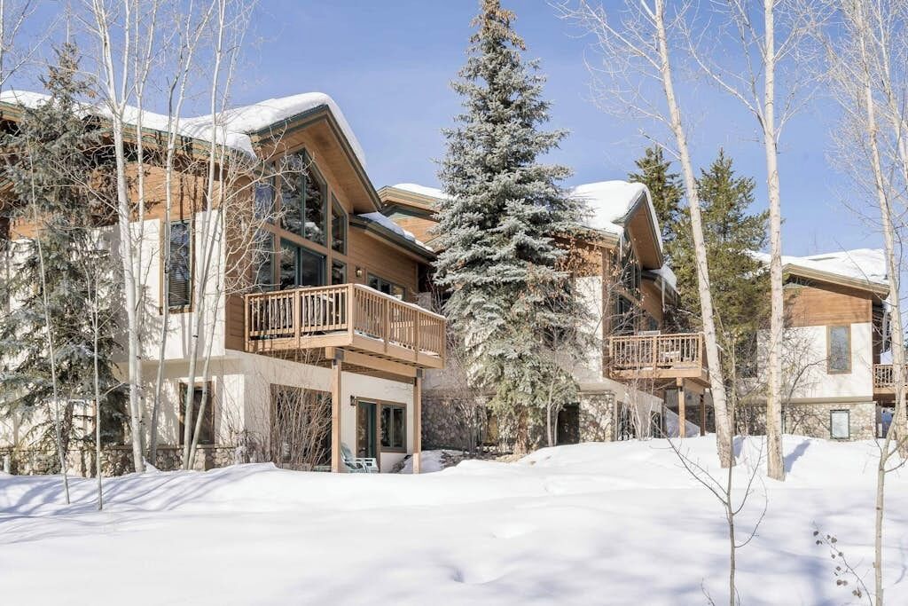 Un chalet enneigé doté de plusieurs balcons, avec un grand arbre à feuilles persistantes en premier plan.