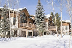 Eine schneebedeckte Lodge mit mehreren Balkonen und einem großen immergrünen Baum im Vordergrund.