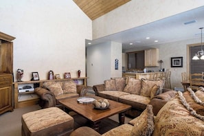 Ein geräumiges Wohnzimmer mit einer großen Eckcouch, einem Holztisch und einer Küche im Hintergrund.