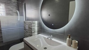 A modern bathroom with a large sink, a toilet, and a mirror with a circular light. - Charming 3-bedroom, 2-bathroom house with AC in quiet neighborhood in Curaçao (Willemstad)